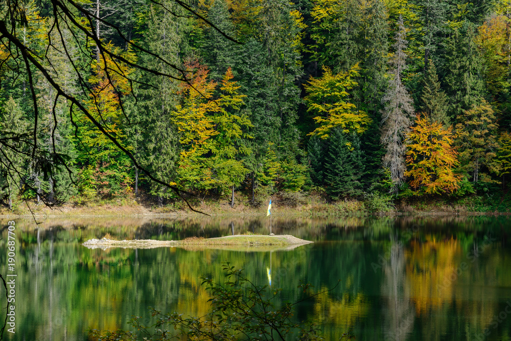 View of Synevir high-altitude lake by autumn day. The leaf fall forest is reflected in water of lake.