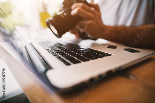 Very close shot of laptop and professional camera in male hands working with it-