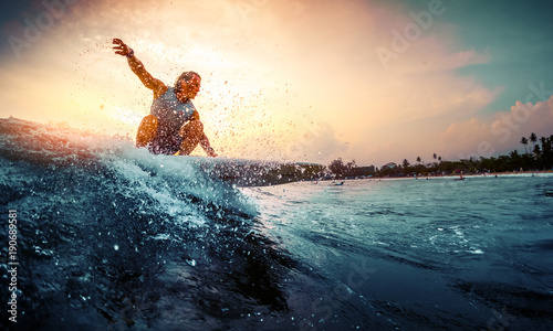 Young surfer rides the wave during sunset