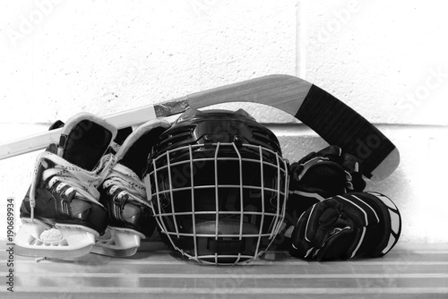 Black and white photo of kid's hockey gear: helmet, stick, gloves, skates