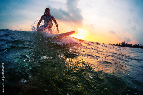 Surfer trying to catch the ocean wave during sunset. Active lifestyle and extreme sport concept