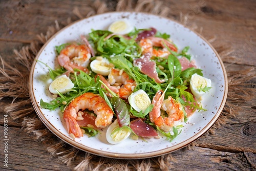 Healthy salad with shrimps, arugula, Parma ham, quail eggs and parmesan cheese.