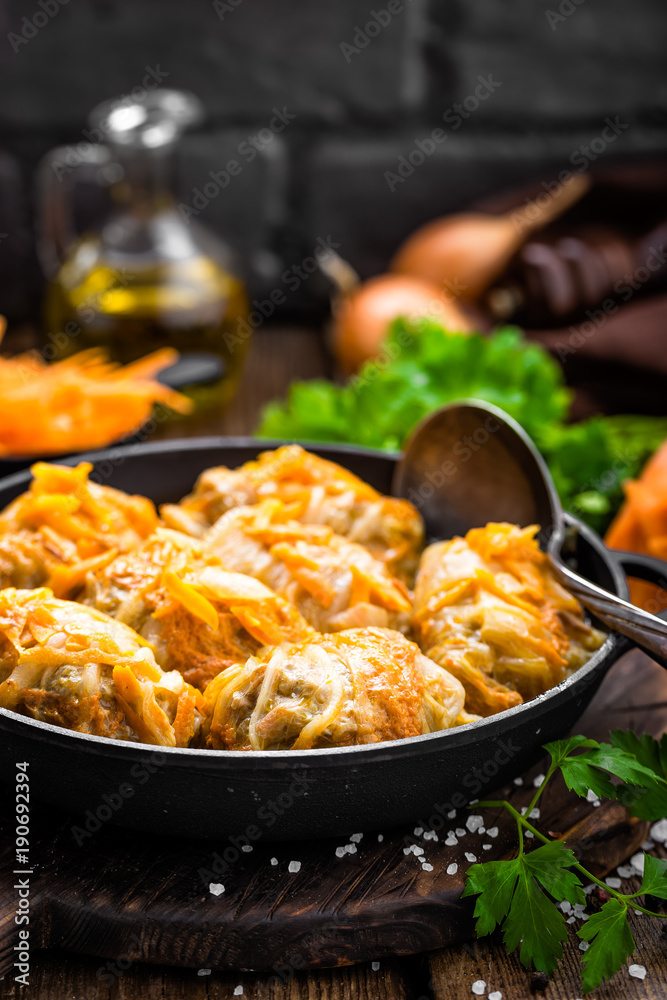 Cabbage rolls stewed with meat and vegetables in pan on dark wooden background