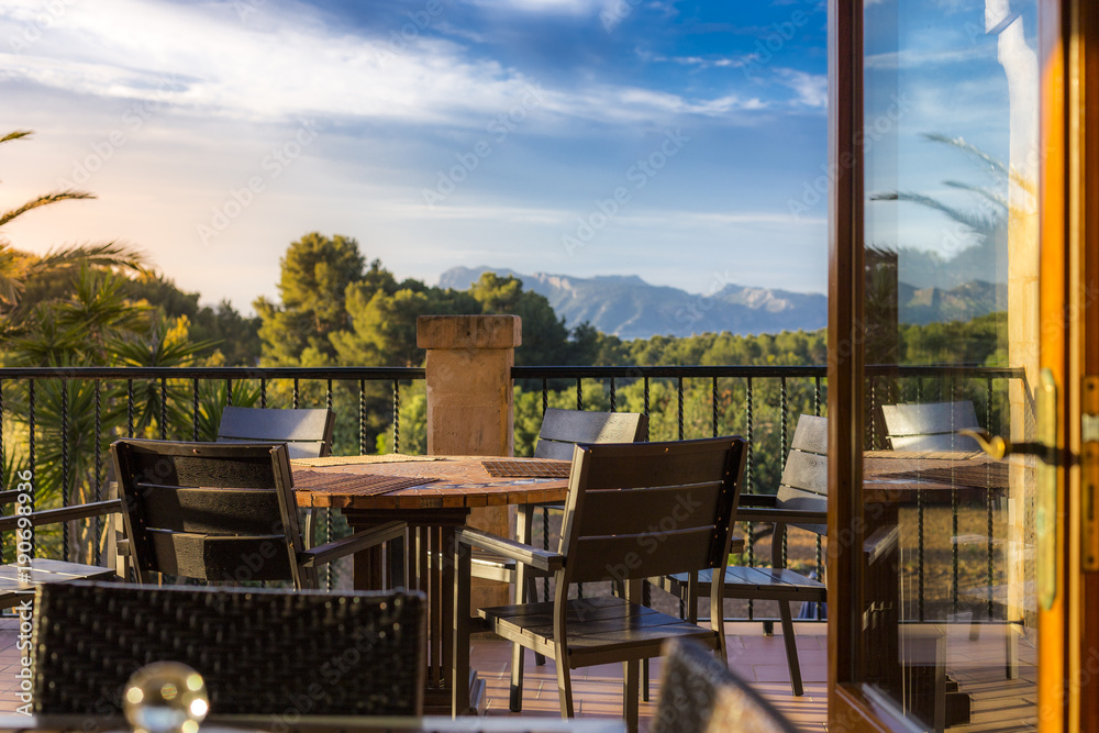 A few chairs and tables on a mediterranean style balcony with a marvellous view over beautiful summer landscape and mountains in the background
