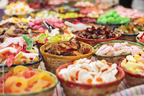 Close up of bowls filled with a large selection of different colourful soft candies including worms, gummy bears, gummy colas, gummy rings etc in a candy shop or a food market