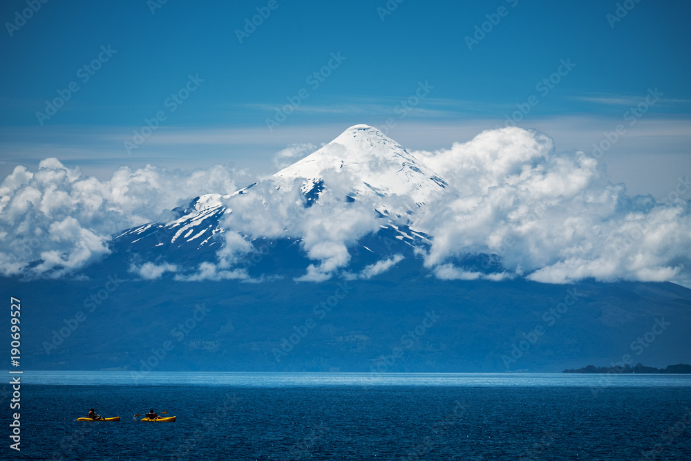 Two explorers paddling kayaks on the lake with volcano on the background. Volcano of Osorno, Chile