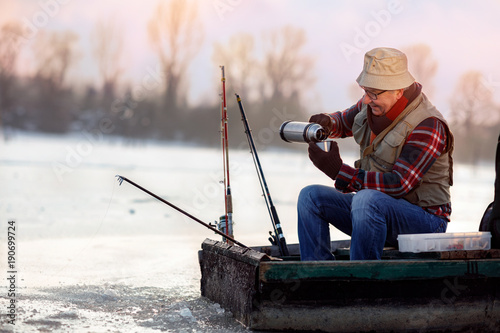 Ice fishing. Fisherman sitting on frozen lake and drink tea