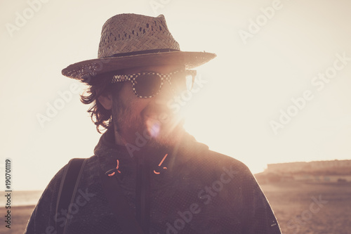 man with straw hat and beard on the beach at sunset looks and smiles and smiles