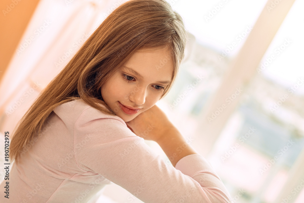 Nice morning. The close up of a charming teenage girl sitting in her bedroom and stretching herself, having woken up not so long ago