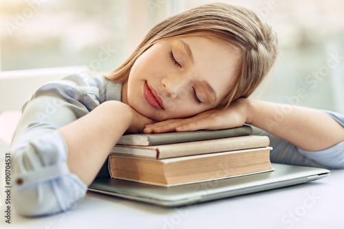 Sweet rest. Charming teenage girl taking a nap while sitting at the table and resting her head on the hands folded on a pile of books