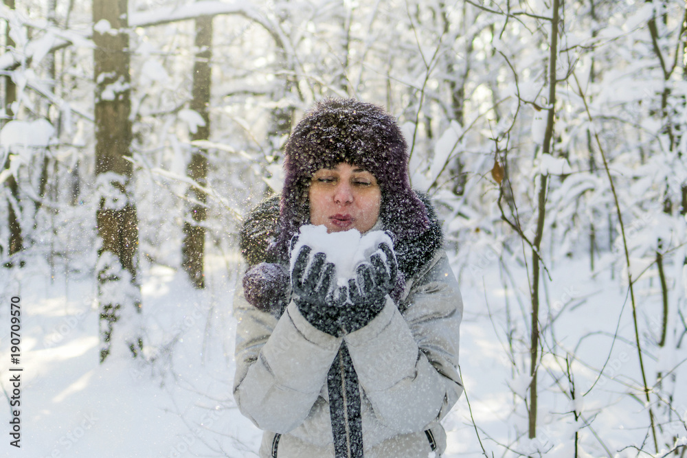 Obraz premium A woman holds a handful of snow in her hands and blows on it. Winter in the forest. The sun sparkles.