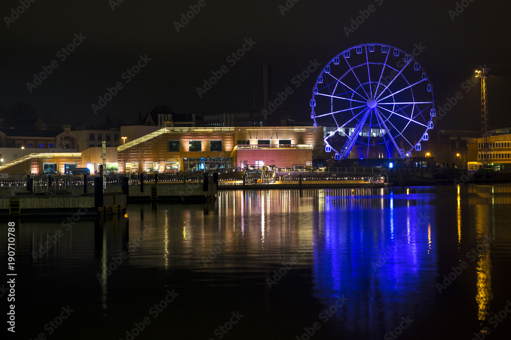 Panorama of the waterfront in Helsinki, Finland, during the long winter night. A ferris wheel and the yellow lights of the buildings are reflected on the water of the sea Panorama of the waterfront in Helsinki, Finland, during the long winter night. A ferris wheel and the yellow lights of the buildings are reflected on the water of the sea