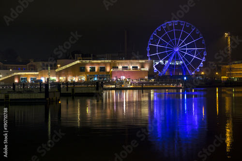 Panorama of the waterfront in Helsinki, Finland, during the long winter night. A ferris wheel and the yellow lights of the buildings are reflected on the water of the sea