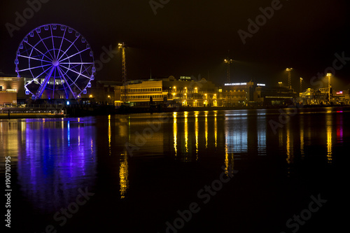 Panorama of the waterfront in Helsinki, Finland, during the long winter night. A ferris wheel and the yellow lights of the buildings are reflected on the water of the sea © Stefano Tammaro