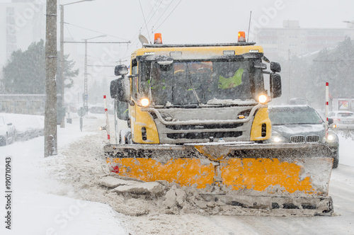 Plow truck cleaning street in the city during rush hour. Street maintenance in winter