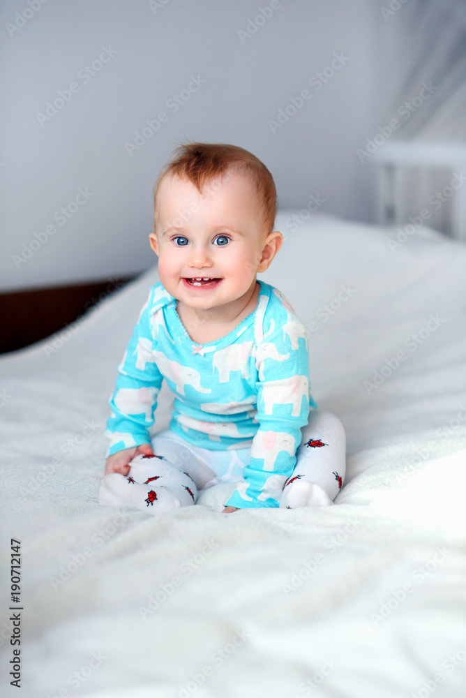 Cute smiling baby sitting on the white blanket at the bed Cute smiling baby sitting on the white blanket at the bed