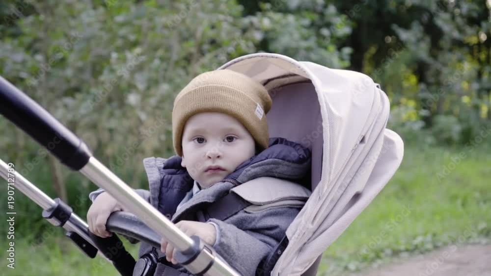 Mom takes the baby in a stroller. A child looks at the camera Mom takes the baby in a stroller. A child looks at the camera