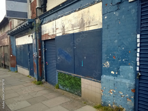 a row of abandoned stores with boarded up shop fronts with crumbling facades and peeling blue paint in an urban street