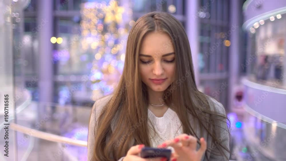 Young woman surfs internet or texting sms message using modern smartphone over blurry big mall background. 4 k Young woman surfs internet or texting sms message using modern smartphone over blurry big mall background. 4 k