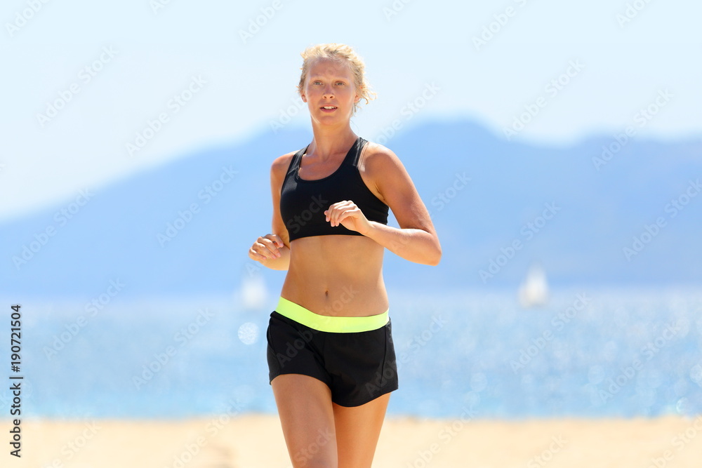 Beautiful blonde girl fitness model running on beach -outdoor workout  getting in shape for the summer. Woman training cardio for weight loss body  concept wearing sports bra and shorts sportswear. Stock Photo