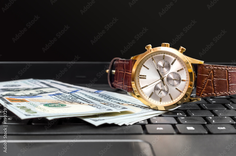 Wrist watch with money on the laptop keyboard.