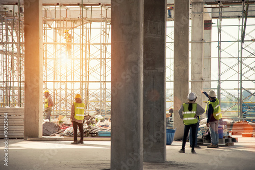 Construction engineers supervising progress of construction project stand on new concrete floor top roof and crane background photo