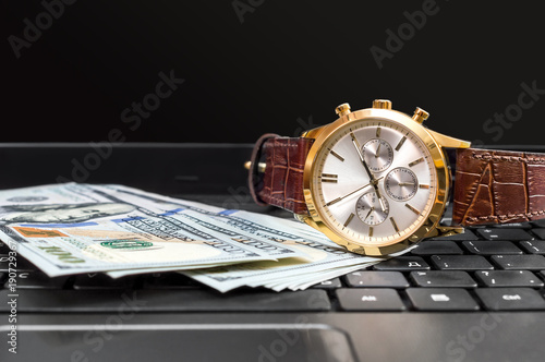 Wrist watch with money on the laptop keyboard.