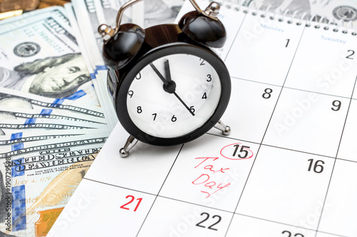 Tax time concept. Alarm clock on the calendar with money.