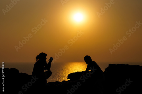 Silhouette of young woman take a picture of his boyfriend in the background of sunset at the sea