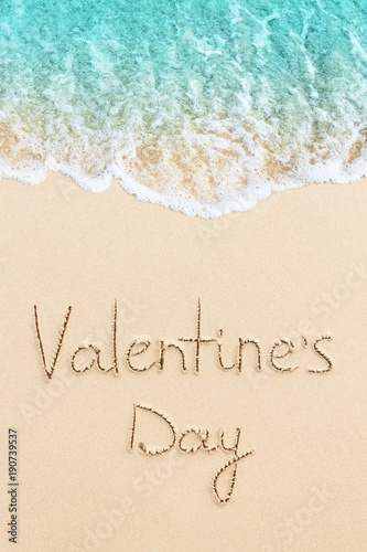 Valentine's Day handwritten on the sand of beach with ocean wave