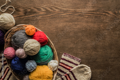 Warm socks created from natural wool for cold weather. Knitting balls in the basket on a brown rustic table. Grandmother made socks for children. Womanly hobby. Knitting concept. Empty place for text.