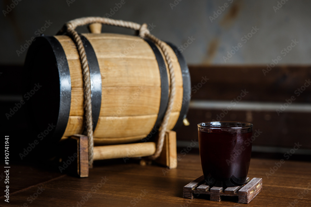 An underexposed horizontal image of a red alcoholic drink in a cocktail glass, on a wooden glass-holder on a table, a wooden barrel near by. Selective focus. An underexposed horizontal image of a red alcoholic drink in a cocktail glass, on a wooden glass-holder on a table, a wooden barrel near by. Selective focus.