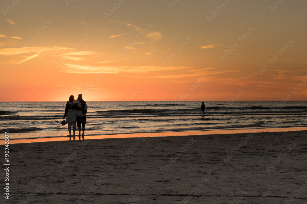 Strandurlaub - verliebtes Paar bestaunt malerischer Sonnenuntergang am Strand Strandurlaub - verliebtes Paar bestaunt malerischer Sonnenuntergang am Strand
