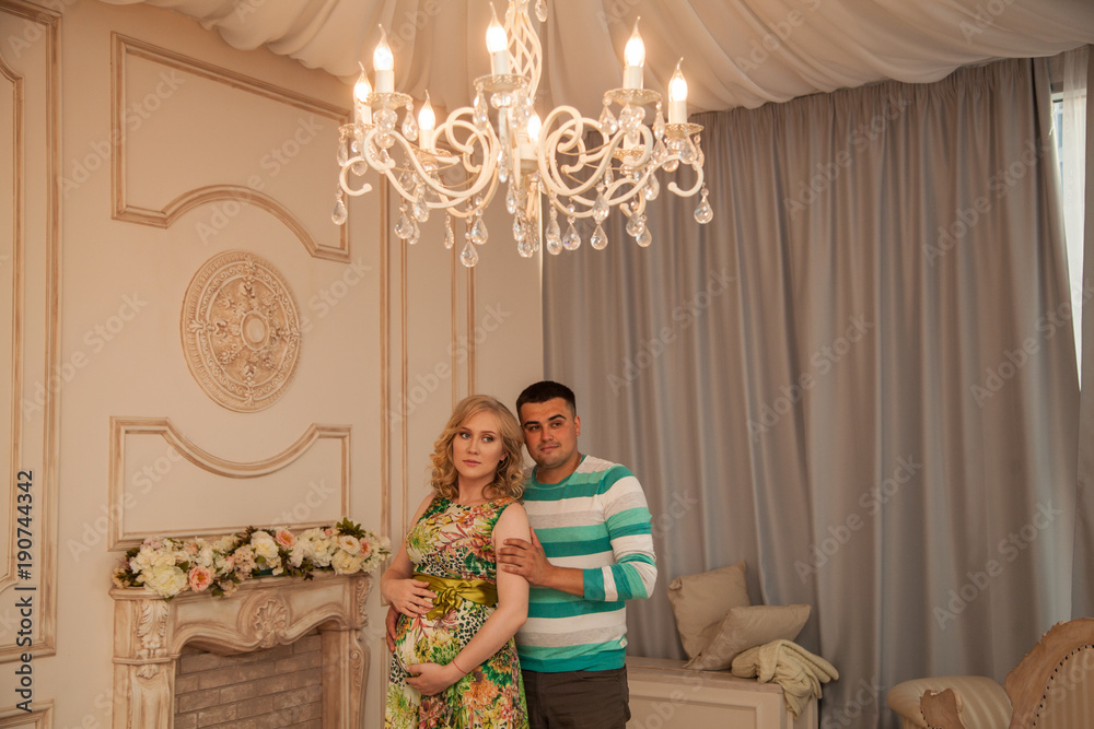 beautiful family couple in anticipation of a child. Beautiful interior. Gentle embrace beautiful family couple in anticipation of a child. Beautiful interior. Gentle embrace