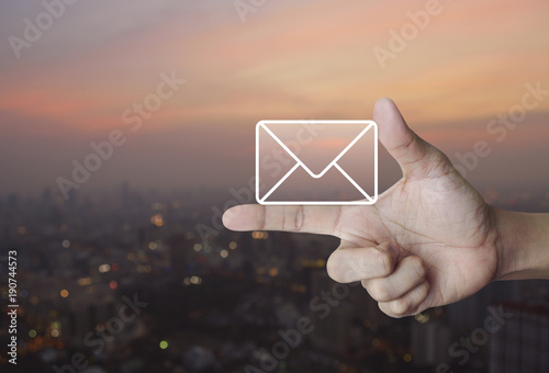 Mail icon on finger over blur of cityscape on warm light sundown, Contact us concept
