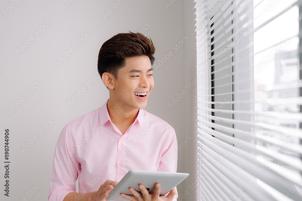 Handsome asian man standing with digital tablet on gray background Handsome asian man standing with digital tablet on gray background