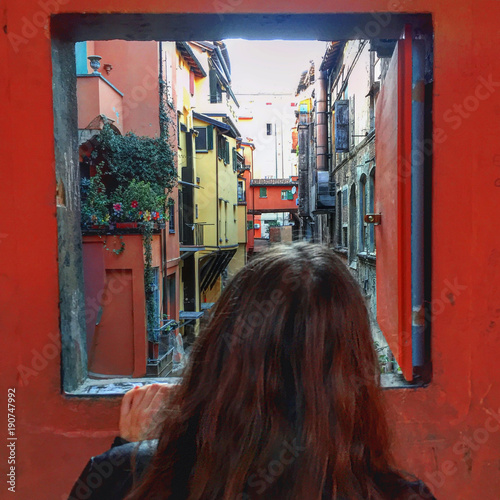 A girl looks through the famous window in Via Piella, Bologna, to the multicoloured houses.  photo