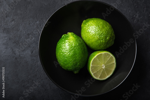 close up of fresh green lime in black bowl, dark background