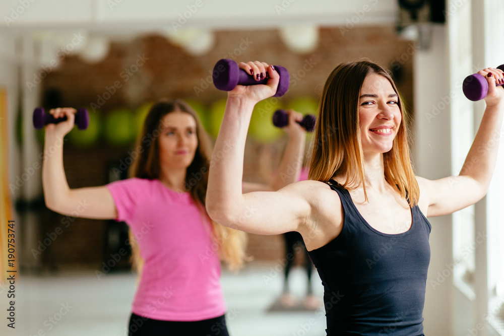 Happy two young women doing exercise with dumbbells in front of the window. Happy two young women doing exercise with dumbbells in front of the window.