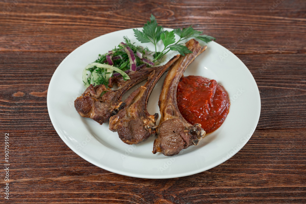 Roasted lamb ribs on a plate. Appetizing dish on the wooden brown table. Roasted lamb ribs on a plate. Appetizing dish on the wooden brown table.