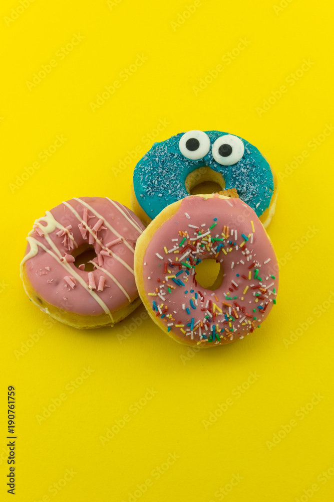 Close-up with many multicolored glazed donuts on yellow background.