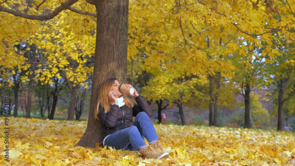 Woman Sitting With His Back To Tree In Yellow Autumn Leaves, Talking Smartphone Woman Sitting With His Back To Tree In Yellow Autumn Leaves, Talking Smartphone