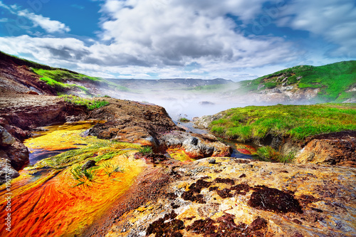 Scenic view of a geothermal area with very colorful deposits, a steaming hot water lake, in the background a mountain range, above a blue sky with a cloud formation - Location: Iceland, Hengill area photo