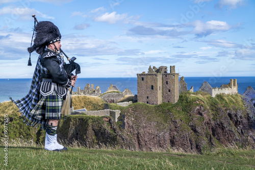 Traditional scottish bagpiper in full dress code at Dunnottar Castle in Stonehaven