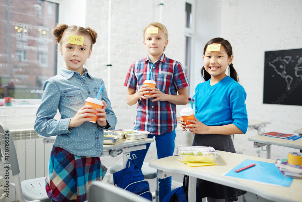 Group of schoolkids with notepapers on their foreheads holding glasses with drinks Group of schoolkids with notepapers on their foreheads holding glasses with drinks