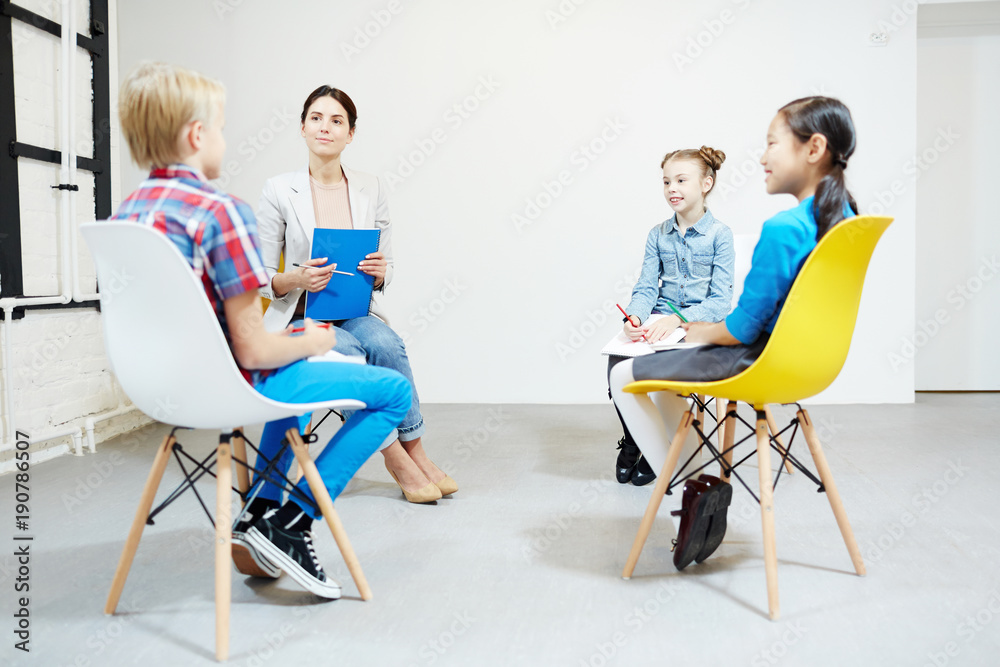 Fototapeta premium Little schoolgirls and young teacher listening to report of clever boy at seminar