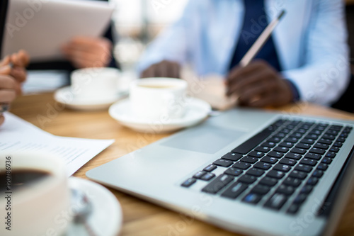 Keypad of laptop on background of cups of coffee and hands of business people during meeting