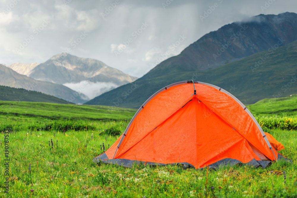 A bright orange tent is set on a beautiful lawn in the mountains, the concept of a relaxed outdoor recreation A bright orange tent is set on a beautiful lawn in the mountains, the concept of a relaxed outdoor recreation