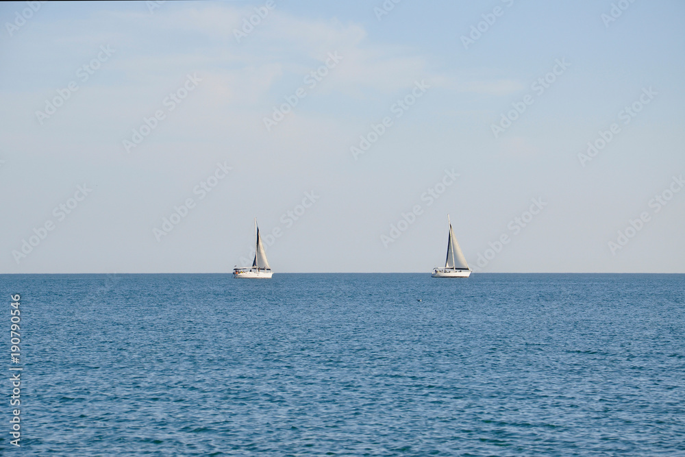 Two white sailboats against the blue sea in the evening light.