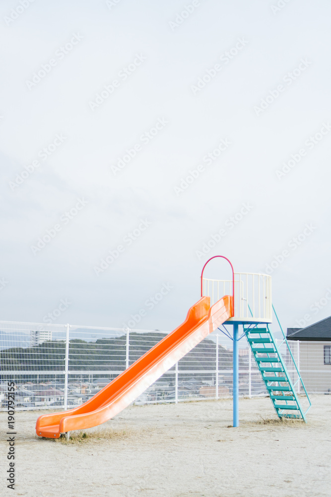 A slide in the playground with nobody on it while the weather is cloudy.